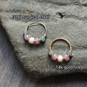 May include: Two hoop earrings with a row of pastel green, pink, and white beads. The hoop on the left is made of 316L surgical steel, and the hoop on the right is made of 14k gold filled.
