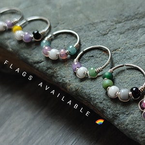 May include: A set of seven silver hoop earrings with colorful beads. Each hoop has a different color combination of beads, including purple, green, white, black, and gray. The text "OTHER FLAGS AVAILABLE" is visible in the image.