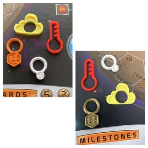 May include: A set of six colorful plastic game pieces, including a yellow cloud, a red thermometer, a white ring, an orange key, a gold key, and a yellow cloud. The pieces are on a game board with the word "MILESTONES" printed on it.