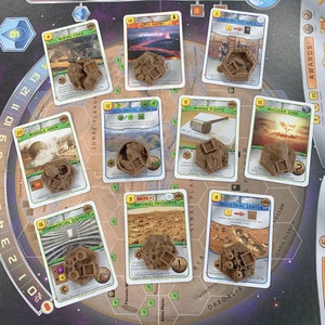 May include: A board game with cards and brown game pieces. The cards have images and text, including "Mining Area," "Lava Flows," and "Ecological Zone." The game pieces are hexagonal and have square cutouts.