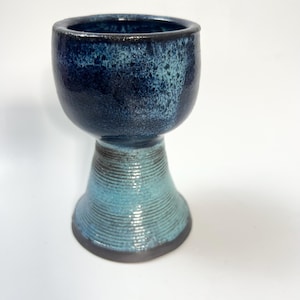 以下が含まれることがあります： 青と黒のセラミック製のゴブレットで、広がったベースがあります。ゴブレットは斑点のある釉薬と滑らかで丸みを帯びた縁を持っています。