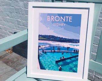 May include: A white framed print with a colorful illustration of a beach scene in Sydney, Australia. The print features the text "Bronte Sydney" in pink letters.
