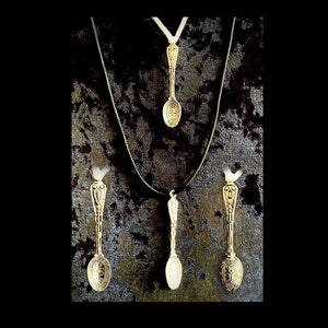 May include: Three gold-tone spoon pendants on black and white fabric. The spoons have ornate designs and are hanging from black and white cords.