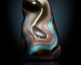 May include: A polished, oblong gemstone with swirling patterns of brown, blue, and tan. The stone has a glossy finish and is set against a dark background. The word "STELLA" is displayed at the bottom.