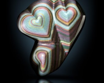 May include: A multi-colored heart-shaped stone with a swirling pattern of pink, green, blue, and gold. The stone is polished and has a glossy finish. The text "STELLA NEW YORK" is visible on the stone.