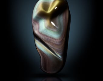 May include: A polished, iridescent gemstone with swirling patterns of gold, brown, and blue. The stone has a smooth, rounded shape and reflects light, creating a shimmering effect. The word "STELLA" is printed at the bottom.