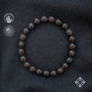 May include: A dark red gemstone bracelet with round beads. The bracelet is made of natural stones and is handmade in the USA.