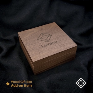 Peut inclure: Une bo&icirc;te cadeau carr&eacute;e en bois avec une finition marron fonc&eacute;. Le couvercle de la bo&icirc;te pr&eacute;sente un motif g&eacute;om&eacute;trique et le nom "Luxane" grav&eacute;. La bo&icirc;te est pos&eacute;e sur un fond sombre et textur&eacute;.