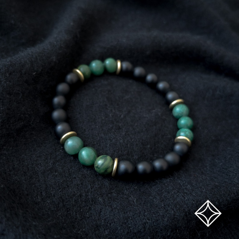 May include: A black and green beaded bracelet with gold accents. The bracelet is made with round beads and has a simple design.
