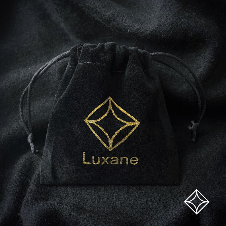 May include: A black velvet pouch with a gold drawstring closure. The pouch has a gold logo with a diamond shape and the word "Luxane" printed below it.