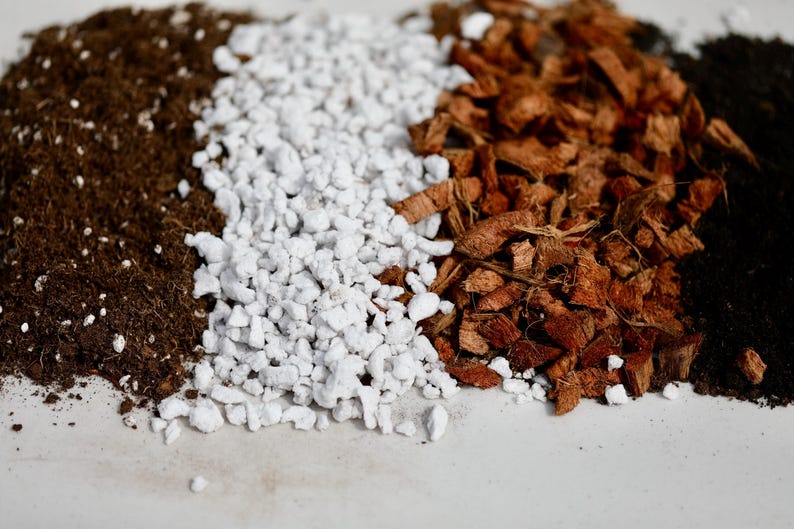 May include: Close-up of four different types of soil: dark brown soil, white perlite, brown coconut coir, and black soil.