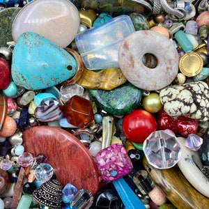 May include: A large assortment of colorful and textured beads, stones, and other jewelry making supplies. The collection includes turquoise, red, brown, white, and green stones, as well as metal charms and beads.