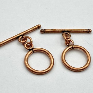 May include: Two gold-toned metal toggle clasps with round rings. Each clasp has a bar that slides through the ring.