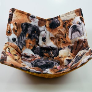 May include: A yellow bowl-shaped pot holder with a pattern of various dog breeds. The fabric is brown, black, and white with a variety of dog breeds, including a bulldog, a rottweiler, and a terrier.