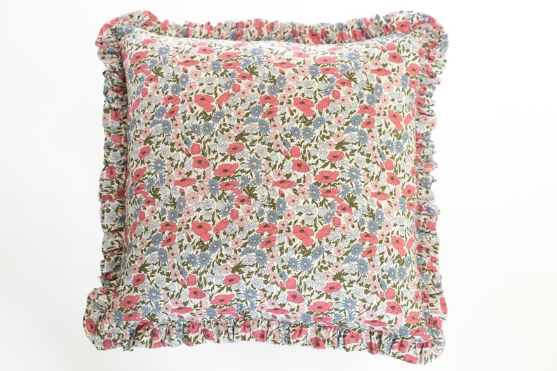 Op de afbeelding: Vierkant kussen met een bloemenpatroon in roze, blauw en groen op een cr&egrave;mekleurige achtergrond. Het heeft een gerimpelde rand voor extra decoratie. Het bloemenpatroon bestaat uit kleine, herhalende bloemen.