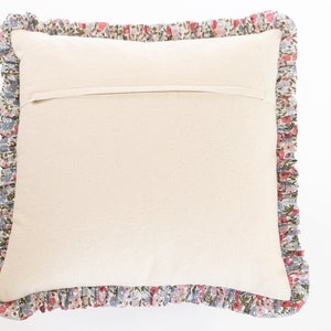 Op de afbeelding: Een vierkant kussen met een cr&egrave;mekleurig midden en een bloemenrand. De ruche heeft een patroon van kleine roze, blauwe en groene bloemen op een witte achtergrond. Het kussen is bedoeld voor decoratief gebruik.