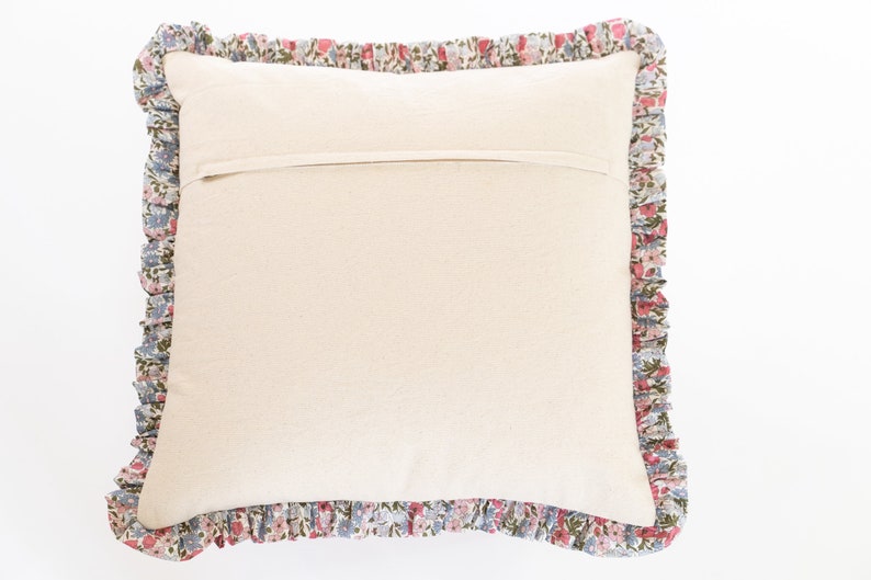 Op de afbeelding: Een vierkant kussen met een cr&egrave;mekleurig midden en een bloemenrand. De ruche heeft een patroon van kleine roze, blauwe en groene bloemen op een witte achtergrond. Het kussen is bedoeld voor decoratief gebruik.