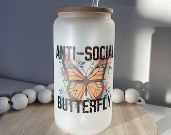 May include: White frosted glass tumbler with a brown lid and a clear drinking straw. The tumbler has a graphic of a butterfly with the text "Anti-Social Butterfly" printed on it.