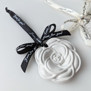 Könnte beinhalten: Weißer Keramik-Rosen-Anhänger mit einem schwarzen Band darum gebunden. Das Band trägt den Text "Just for you".
