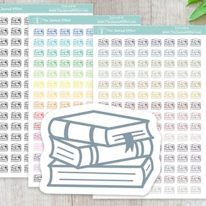 May include: A sheet of stickers with a stack of books design. The stickers are in various colors, including black, white, gray, blue, green, yellow, orange, red, and brown. The stickers are arranged in rows and columns on a white background. The text "The Journal Effect" is printed at the top of the sheet.