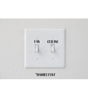 May include: A white light switch plate with two switches labeled "FAN" and "CEILING" in black text. The text "*HASHED FONT" is below the plate. The switches are in the "on" and "off" positions.