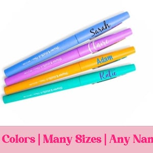 May include: Four colorful pens with custom names: Sarah, Claire, Adam, and Katie. The pens are blue, purple, yellow, and teal. The text at the bottom reads: 50 Colors | Many Sizes | Any Name.