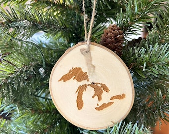 May include: A wooden Christmas ornament shaped like the Great Lakes. The ornament is made of a natural wood slice and has a rustic look.