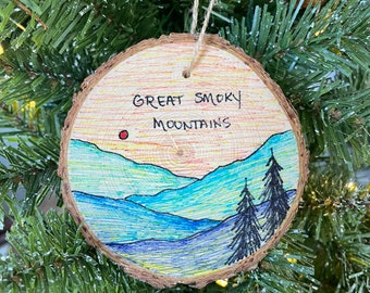 Könnte beinhalten: Ein Holz-Anhänger mit handgemaltem Motiv der Great Smoky Mountains. Der Anhänger ist in Blau-, Grün-, Gelb- und Orangetönen bemalt. Der Text "Great Smoky Mountains" ist in schwarzer Tinte auf den Anhänger geschrieben.
