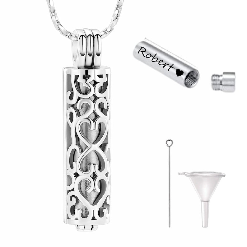 This image showcases a silver filigree cremation pendant with an inner capsule that can be personalized with engraving. It includes a screw-top closure, a small funnel, and a pin for easy filling, making it a meaningful memorial piece for storing ashes or keepsakes.