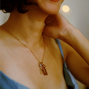 Gold birth flower necklace with engraved floral bar pendants and personalized birthstone charms, elegantly worn by a model. A sentimental and stylish jewelry piece, perfect for celebrating loved ones. Ideal for birthdays, anniversaries, or meaningful gifts.