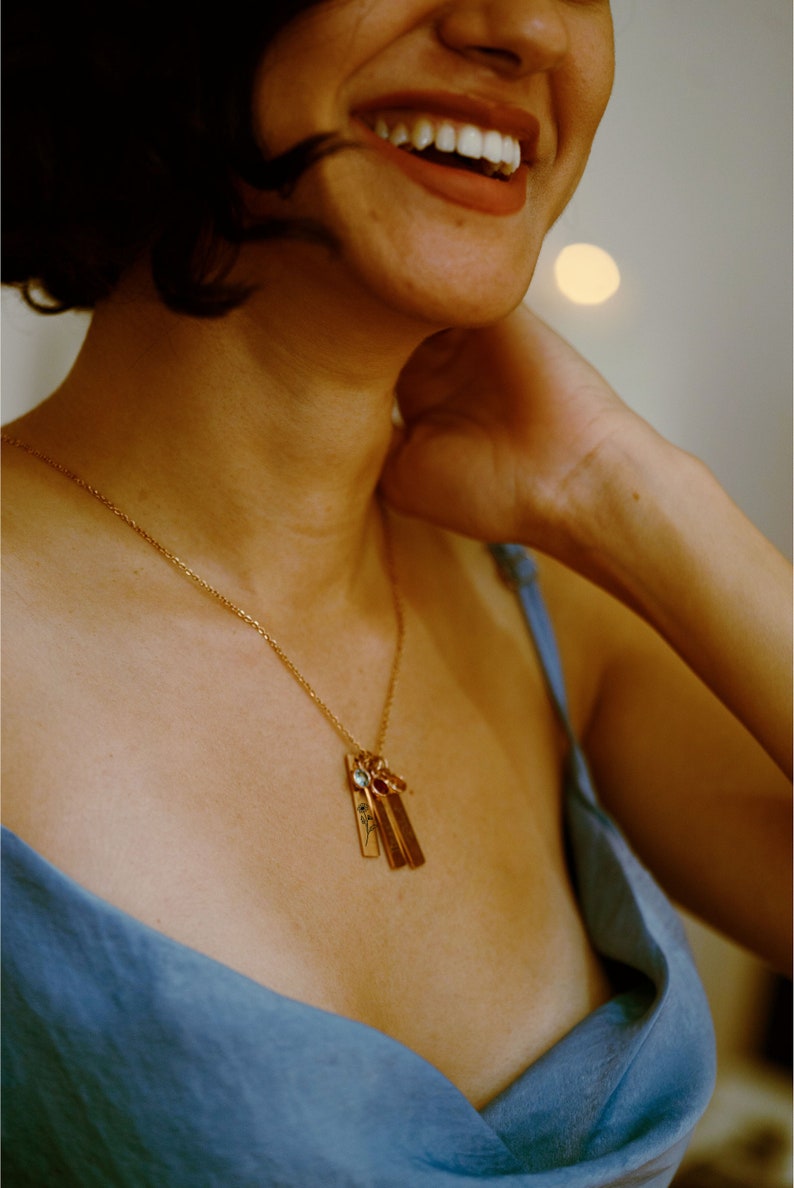 Gold birth flower necklace with engraved floral bar pendants and personalized birthstone charms, elegantly worn by a model. A sentimental and stylish jewelry piece, perfect for celebrating loved ones. Ideal for birthdays, anniversaries, or meaningful gifts.
