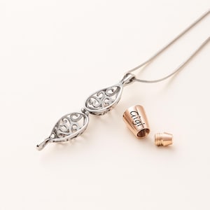 Pu&ograve; includere: Una collana color argento con un ciondolo in filigrana traforata a forma di goccia, accompagnata da un tappo cilindrico color oro rosa inciso con il nome Gigi e un piccolo componente metallico a vite coordinato per la chiusura.
