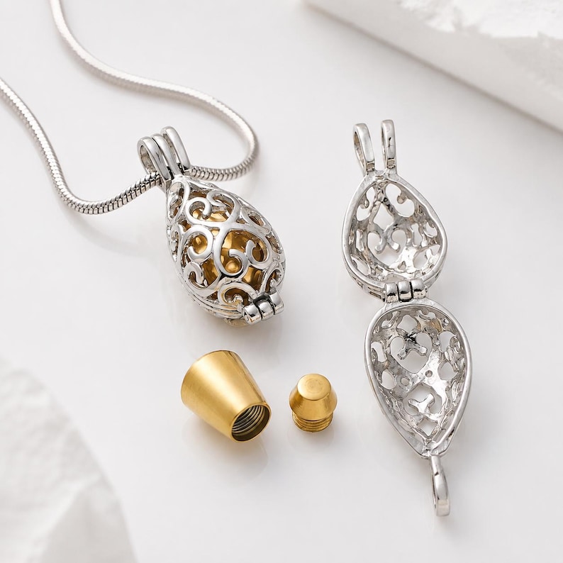 Pu&ograve; includere: Una collana con ciondolo in filigrana color argento caratterizzata da un design a gabbia a forma di goccia che si apre per rivelare una sfera interna color oro. Il set include un tappo conico color oro separato e un piccolo componente a vite.