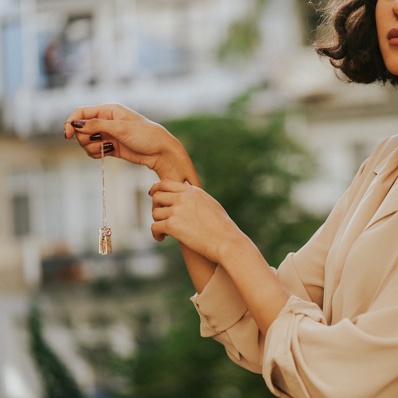 Gold birth flower necklace with engraved bar pendants and birthstone charms, elegantly displayed in an outdoor setting. A meaningful and timeless jewelry piece representing loved ones. Perfect for birthdays, anniversaries, or as a sentimental keepsake gift.