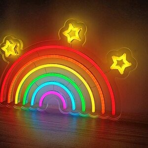 May include: A rainbow neon sign with five layers of color, red, orange, yellow, green, and blue. The sign is shaped like a rainbow arch with three yellow star-shaped lights on top.