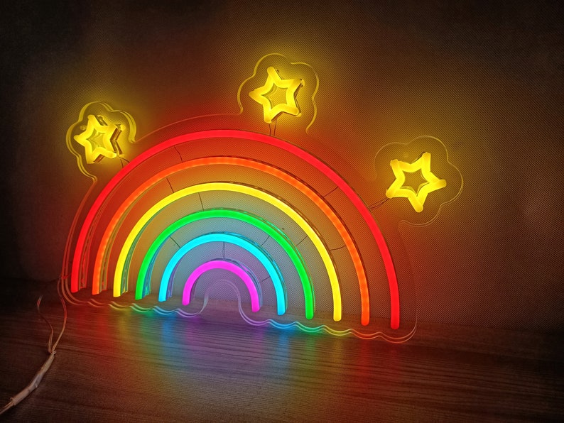 May include: A rainbow neon sign with five layers of color, red, orange, yellow, green, and blue. The sign is shaped like a rainbow arch with three yellow star-shaped lights on top.