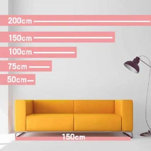 Puede incluir: Un sof&aacute; amarillo con dos cojines, que mide 150 cm de ancho. El sof&aacute; est&aacute; frente a una pared blanca con l&iacute;neas rosas que indican diferentes longitudes en cent&iacute;metros: 200 cm, 150 cm, 100 cm, 75 cm y 50 cm.