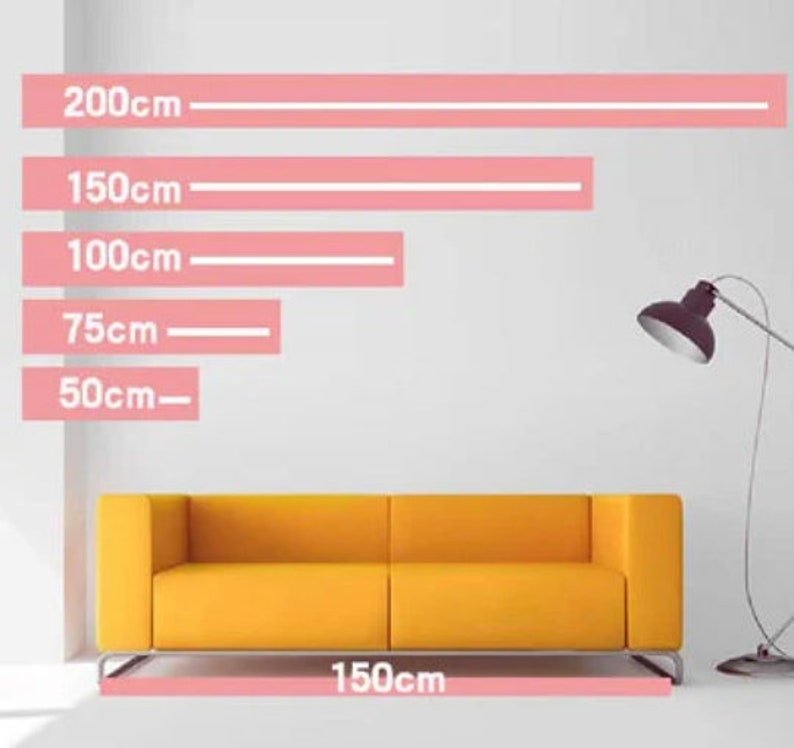 Puede incluir: Un sof&aacute; amarillo con dos cojines, que mide 150 cm de ancho. El sof&aacute; est&aacute; frente a una pared blanca con l&iacute;neas rosas que indican diferentes longitudes en cent&iacute;metros: 200 cm, 150 cm, 100 cm, 75 cm y 50 cm.