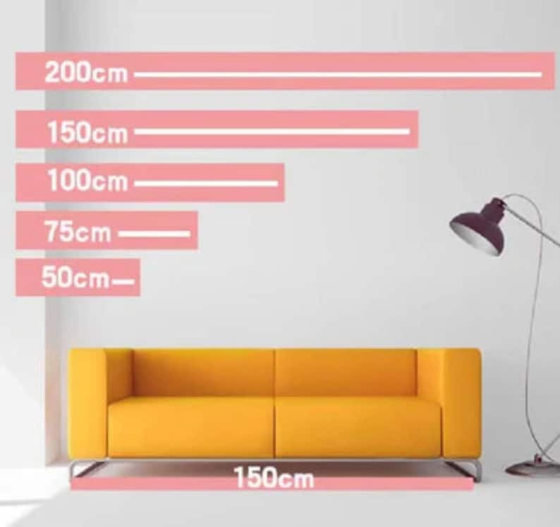 May include: A mustard-yellow sofa with a modern design, shown against a white wall. Pink lines indicate measurements: 50cm, 75cm, 100cm, 150cm, and 200cm. The sofa's base is 150cm long. A dark gray floor lamp is in the background.