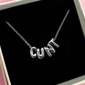 May include: A silver necklace with the word "CUNT" spelled out in bubble letters.