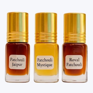 Op de afbeelding: Drie kleine parfumflesjes van glas met goudkleurige doppen. Elke fles bevat een vloeistof van een andere kleur en een etiket met de woorden "Patchouli Jaipur", "Patchouli Mystique" en "Roval Patchouli".