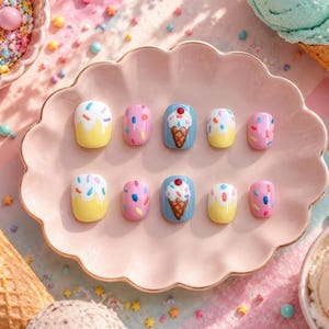 Puede incluir: Un conjunto de diez uñas artificiales con temática de postre. Las uñas presentan diseños de conos de helado, chispas y una base amarilla con chispas blancas y coloridas. Las uñas están dispuestas sobre un plato rosa con volantes.