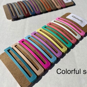 May include: A set of 10 colourful hair clips in various pastel shades, including pink, blue, yellow, and green. The clips are arranged on a brown cardboard backing with the word "Kisamede" printed on it. The text "Colorful set" is printed below the clips.