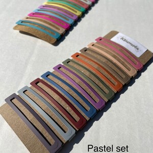 May include: A set of 18 pastel-coloured hair clips on a brown card with the text "Remarkable" and "Pastel set".