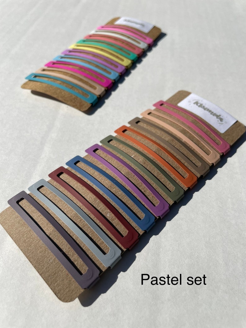 May include: A set of 18 pastel-coloured hair clips on a brown card with the text "Remarkable" and "Pastel set".