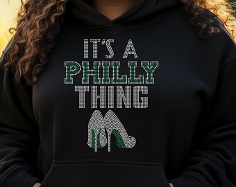 Könnte beinhalten: Schwarzer Hoodie mit einem grünen und weißen Strass-Design, auf dem "It's a Philly Thing" steht, darunter ein Paar High Heels.
