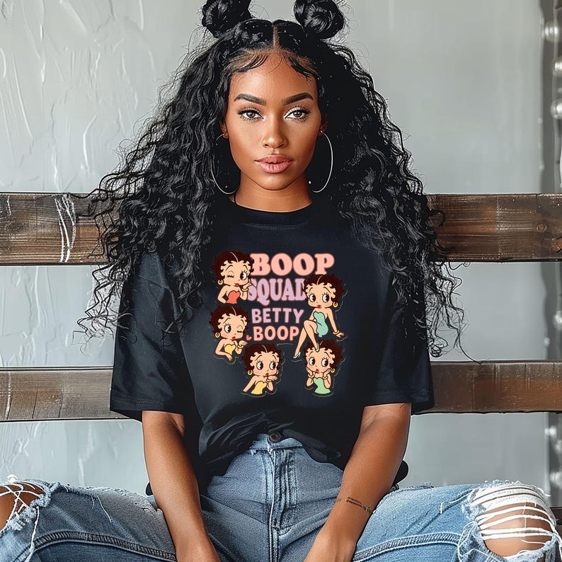 May include: Black t-shirt featuring the text "BOOP SQUAD BETTY BOOP" with multiple Betty Boop cartoon images. The design is in shades of pink, red, yellow, and green. The shirt is made of a soft material.