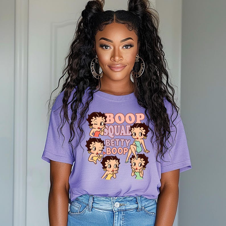 May include: A lavender t-shirt featuring a graphic of Betty Boop and the text "Boop Squad Betty Boop". The design includes multiple Betty Boop illustrations in various poses. The shirt is paired with blue jeans.