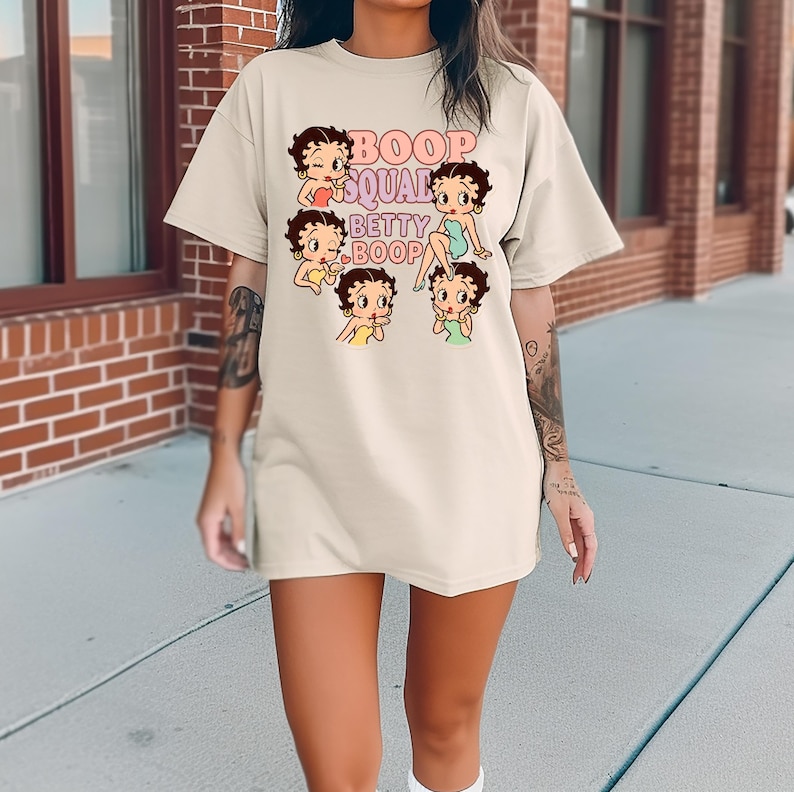 May include: Oversized beige t-shirt featuring a cartoon graphic of Betty Boop and the text "Boop Squad Betty Boop" in pink and purple. The graphic includes multiple Betty Boop illustrations in various poses, with brown hair and colorful outfits.