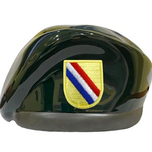 May include: A dark green beret with a yellow patch featuring a red, white, and blue diagonal stripe.
